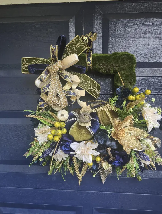 A navy and gold wreath on a navy front door, with cream magnolias, gold ribbon and a square of moss.