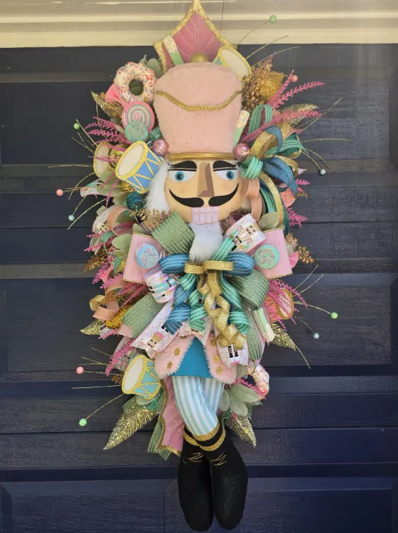 A tall nutcracker door swag in pastel pink and mint, decorated with sweets, doughnuts and lollipops.