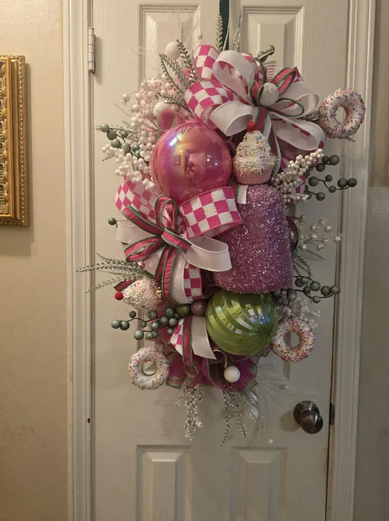 A Christmas door swag in pink and white, with large glass baubles, candy canes and checked ribbon.